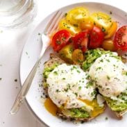 Avocado toast with eggs and yellow and red tomatoes on a plate with a fork.