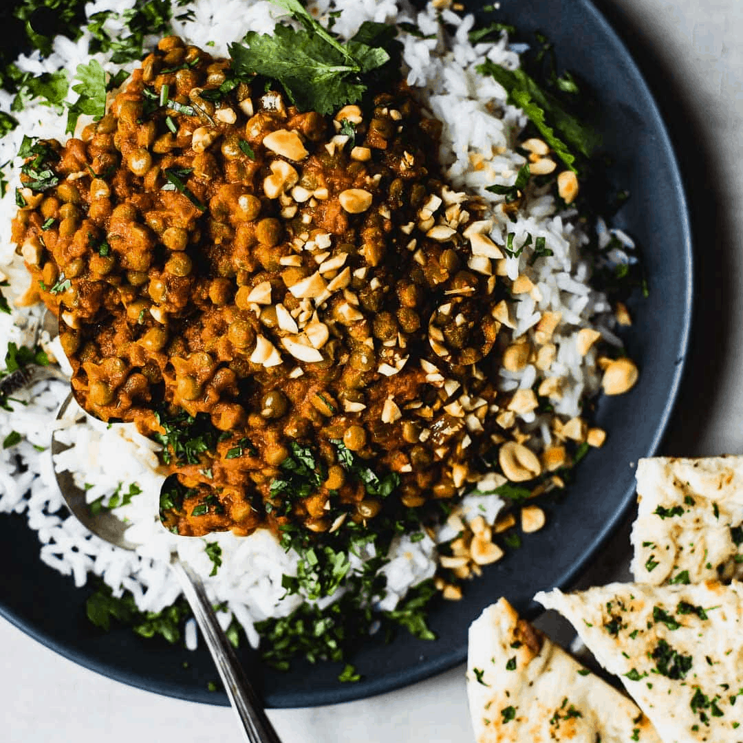 Red curry lentils with rice and bread in a plate with a spoon.