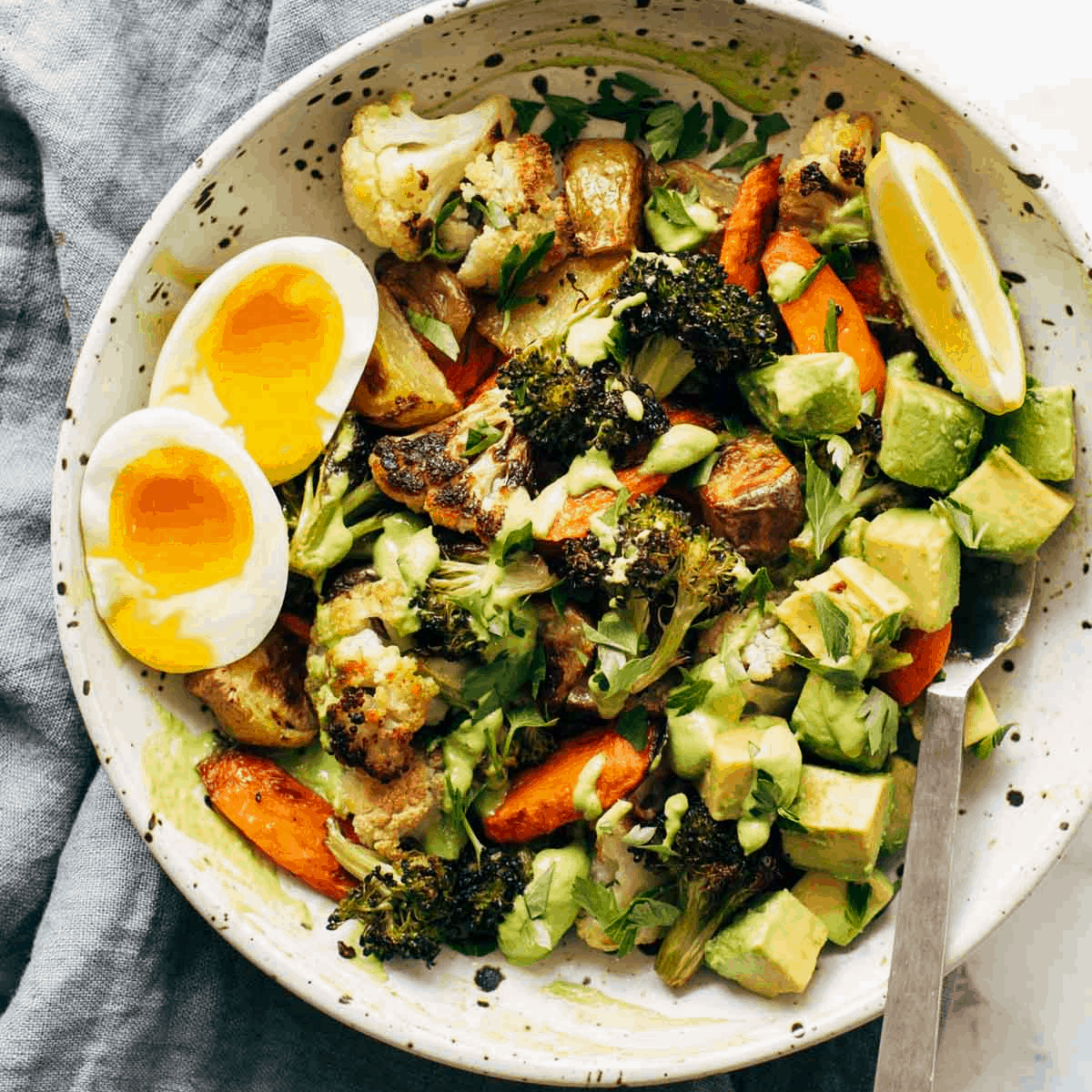 Roasted veggies with avocado, a soft boiled egg on the side, and fresh lemon slices.