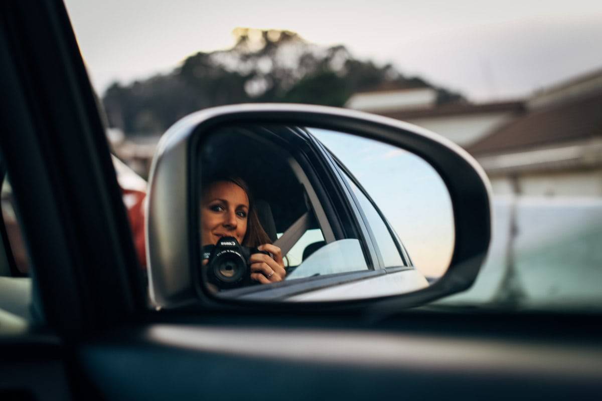 Woman taking a photo in a car mirror.