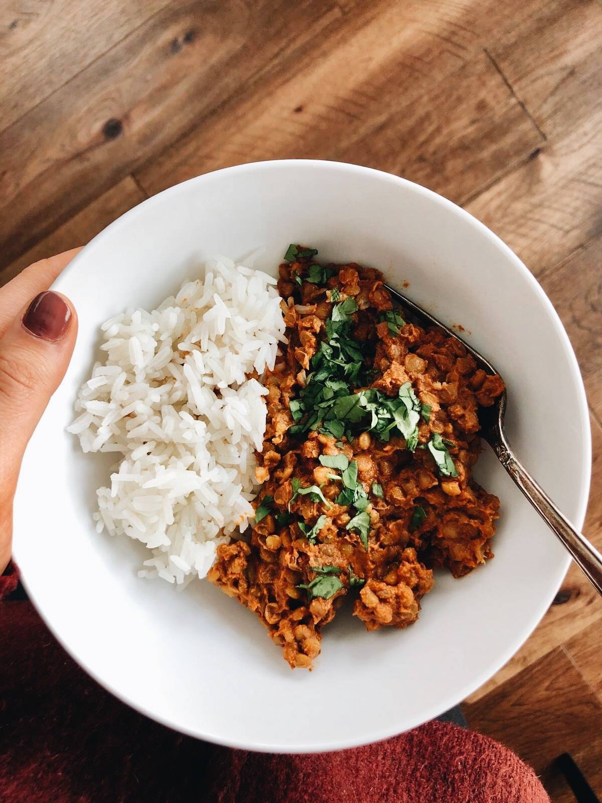 Red Curry Lentils with white rice and cilantro in a white bowl with a fork. 