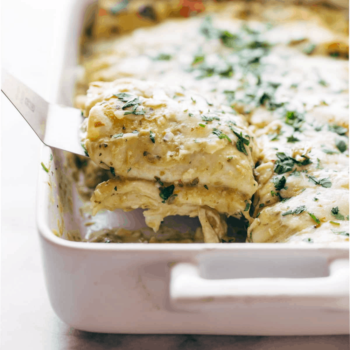 A spatula lifting up enchiladas verdes.