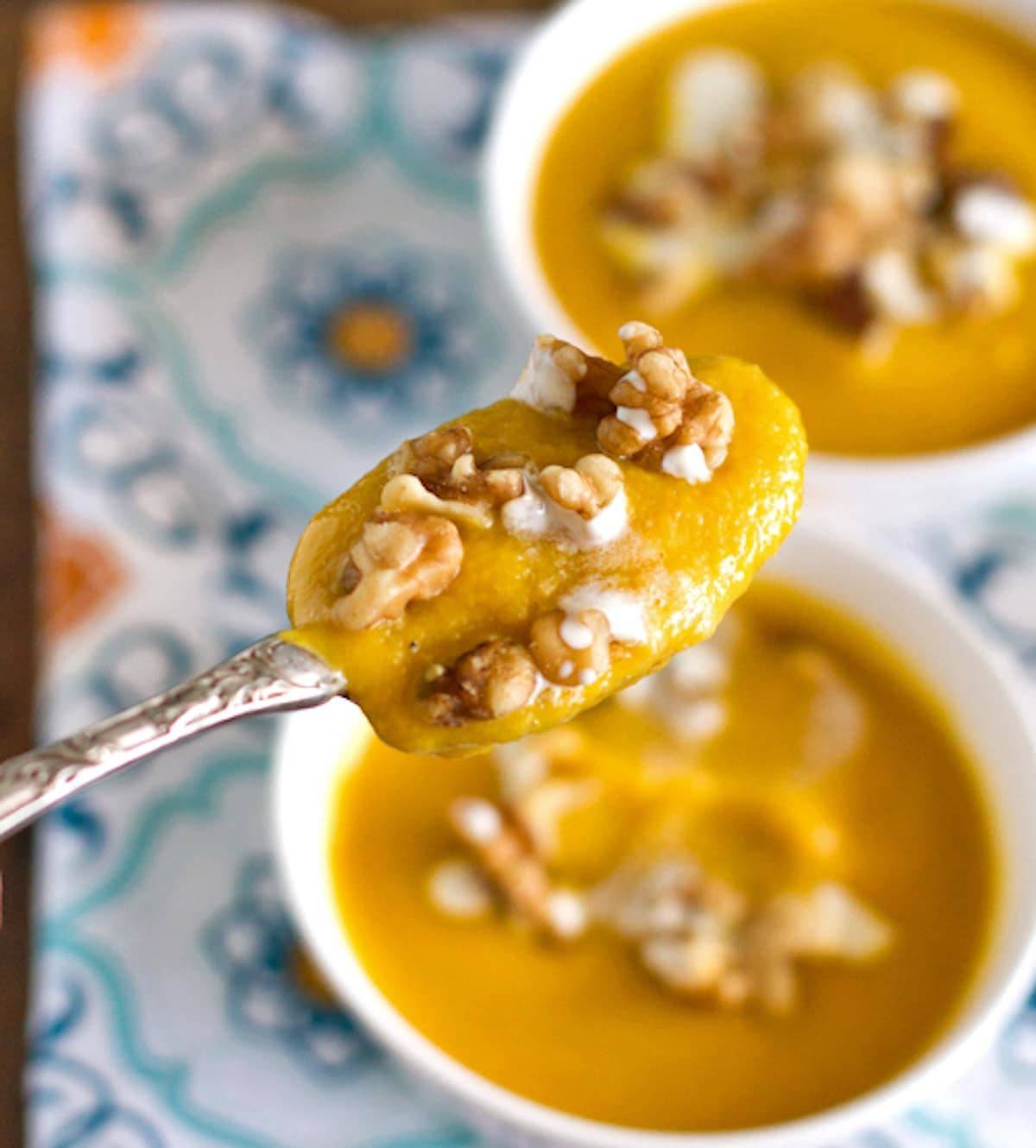 Creamy squash soup on a spoon with toasted walnuts.
