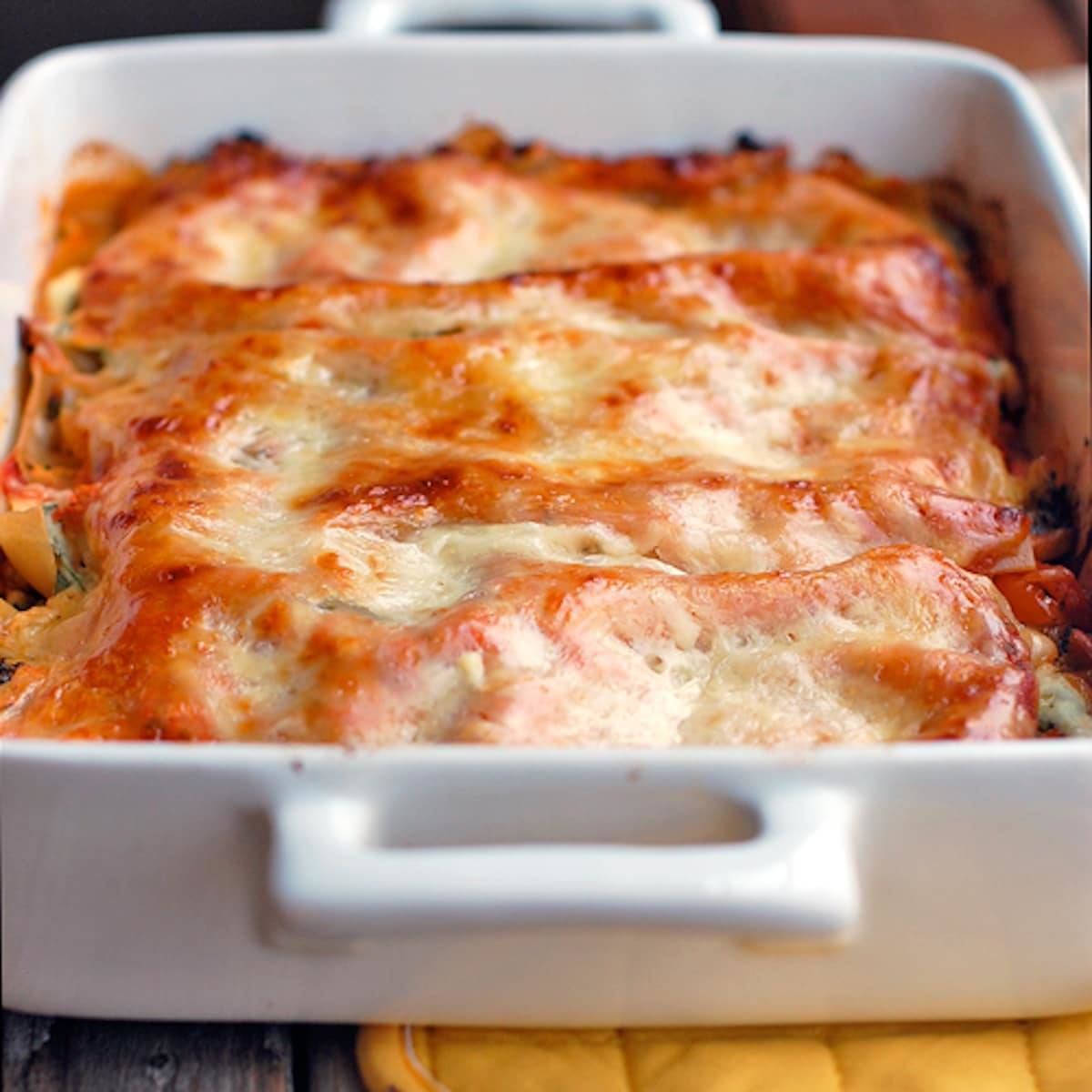 Veggie lasagna full of chopped broccoli, carrots, cauliflower, spinach, ricotta cheese, and tomato sauce in a white baking dish.