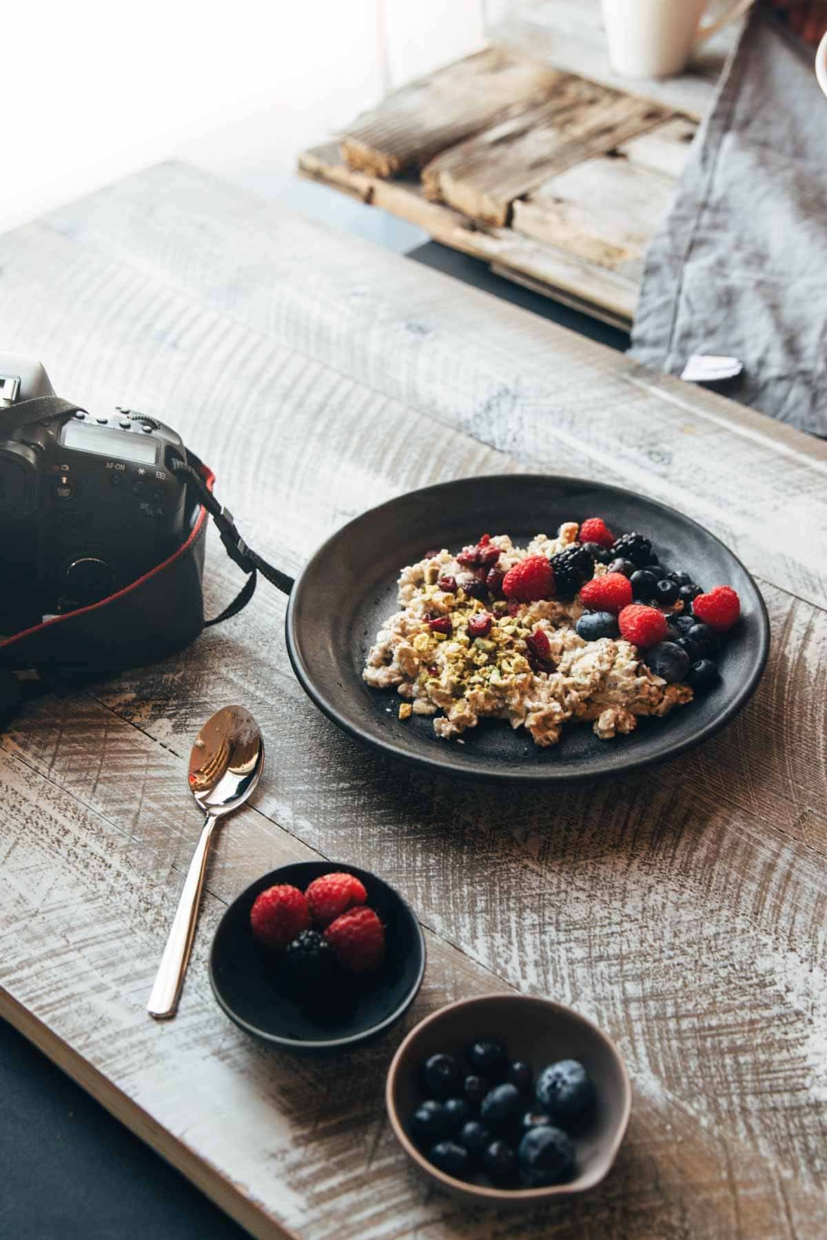Plate with granola and berries with a camera and a spoon.