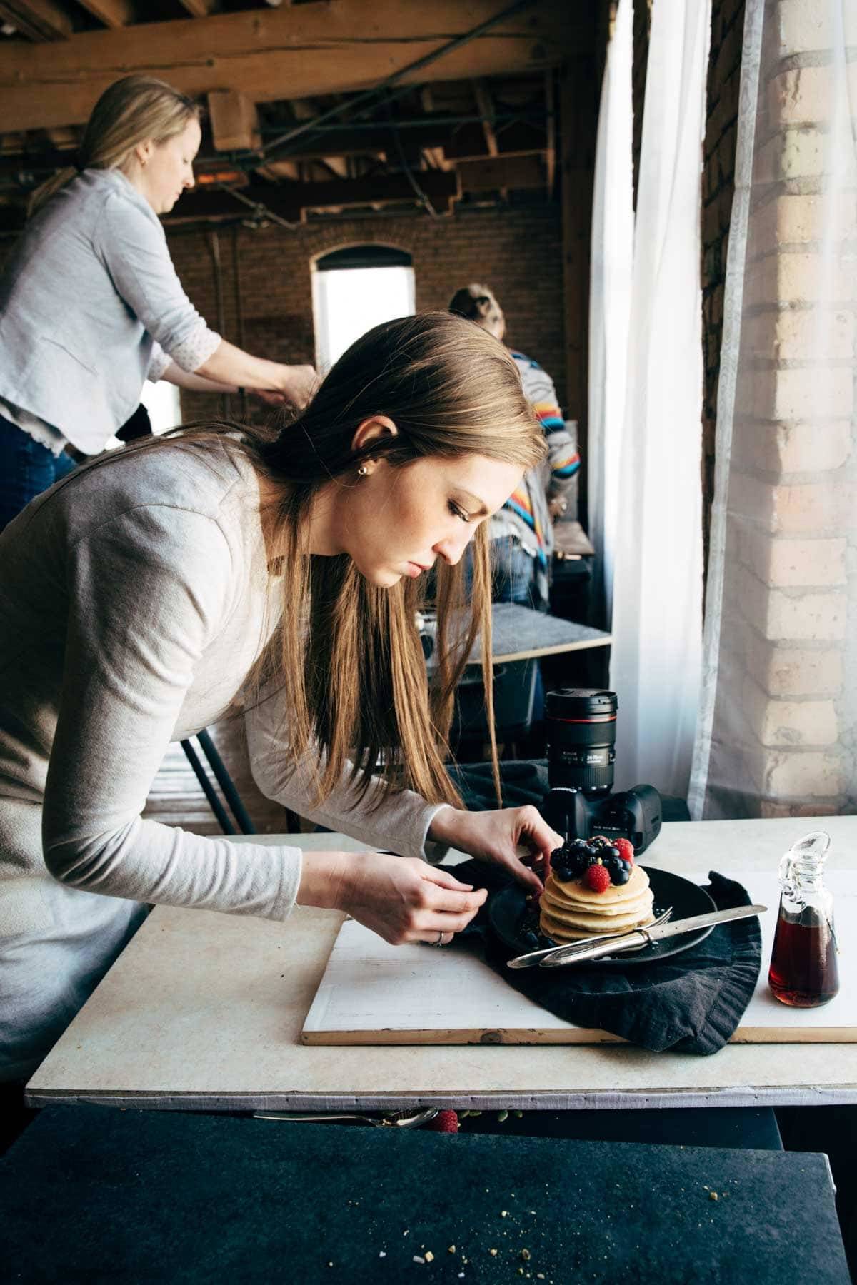 Woman styling pancakes on a plate with a dark napkin.