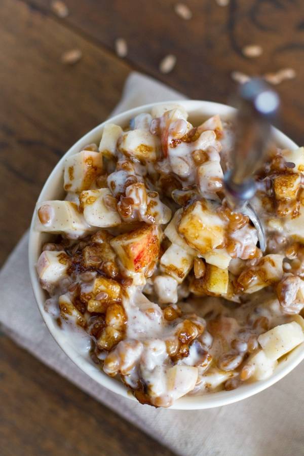 Yogurt parfaits with brown sugar, apples, wheat berries, flax, and walnuts in a bowl with a spoon.